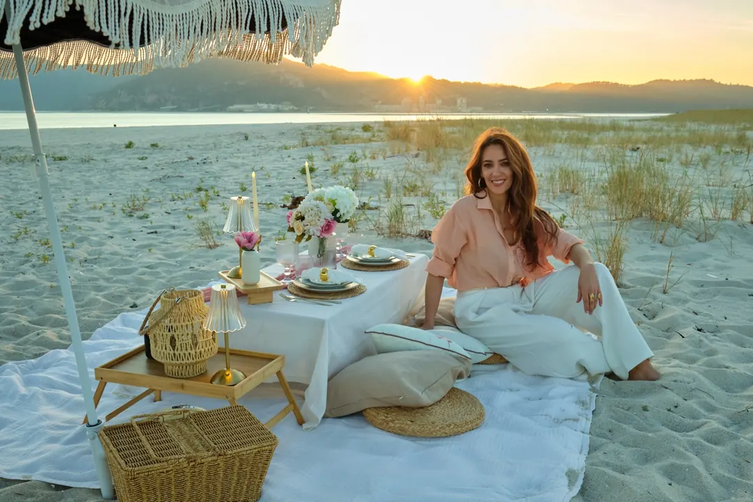 Ana, founder of Picnic Club, beside a picnic she styled on the beach at sunset