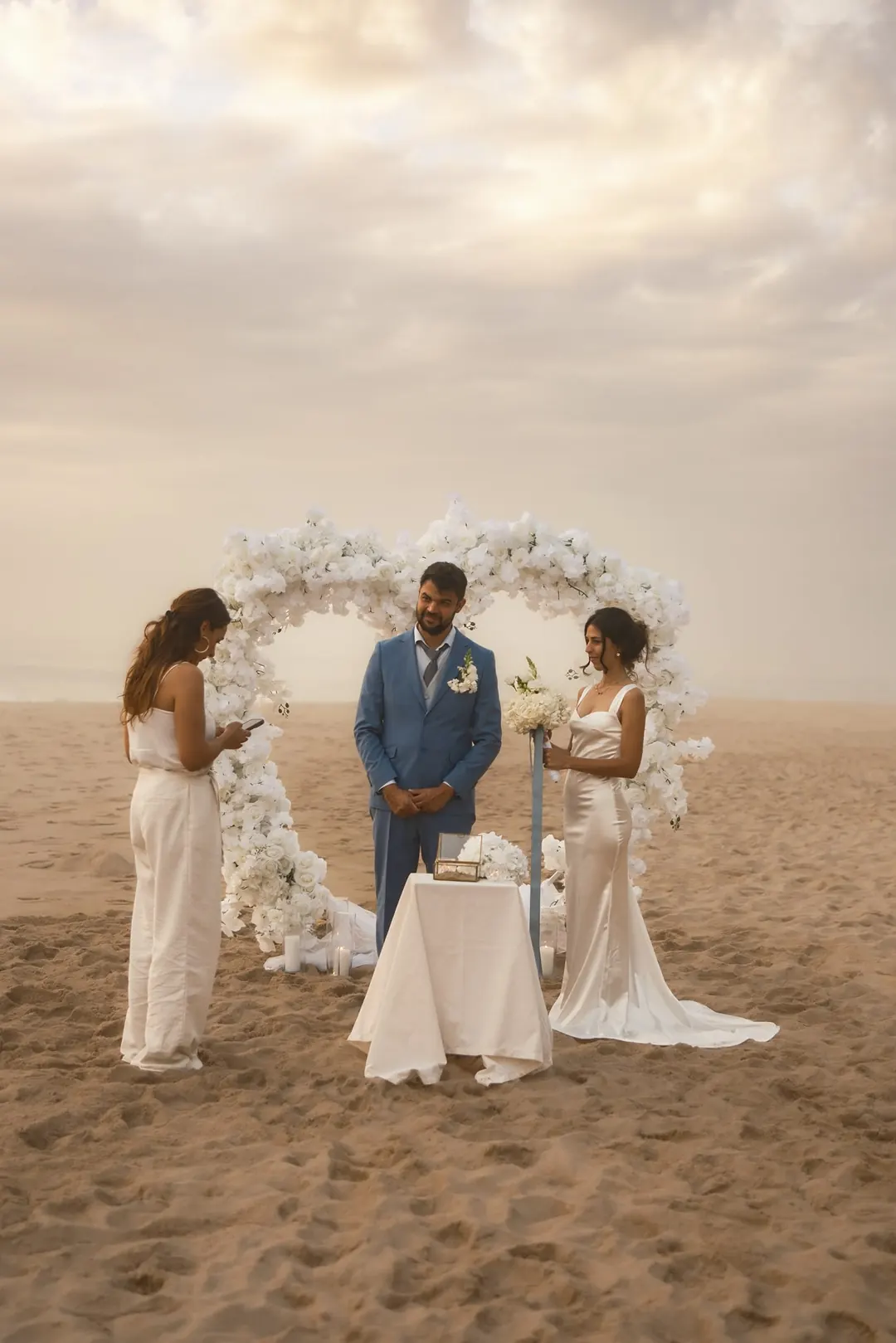 An elopement ceremony on the beach beneath a heart-shaped arch of white flowers