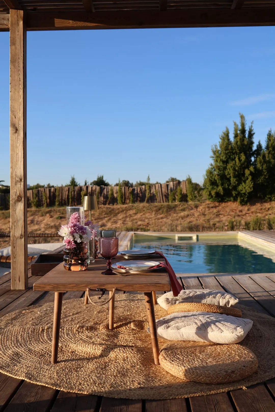 A low table and floor cushions on a deck beside the pool and the pines