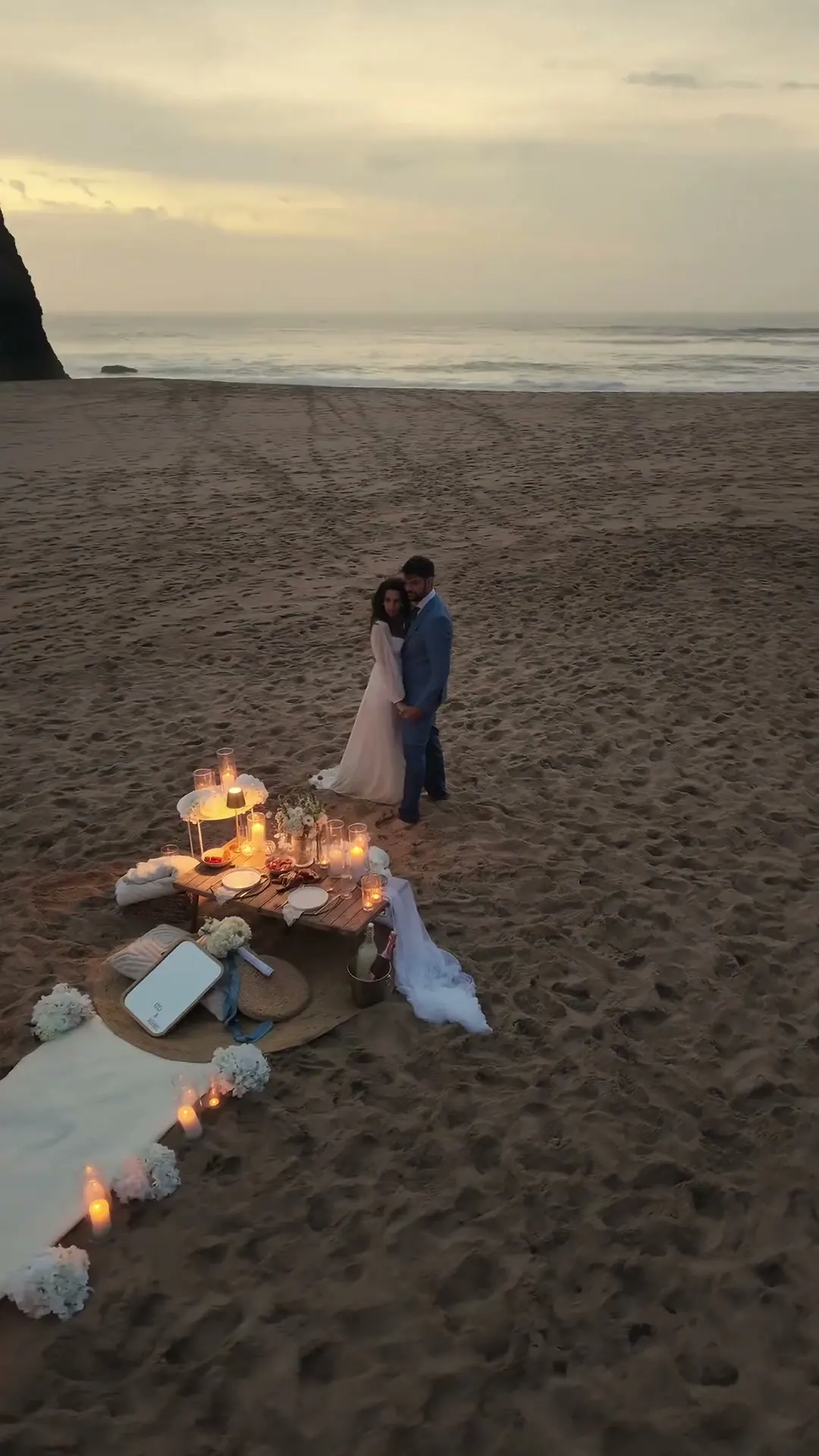 Seen from above: a candlelit table on the sand at dusk