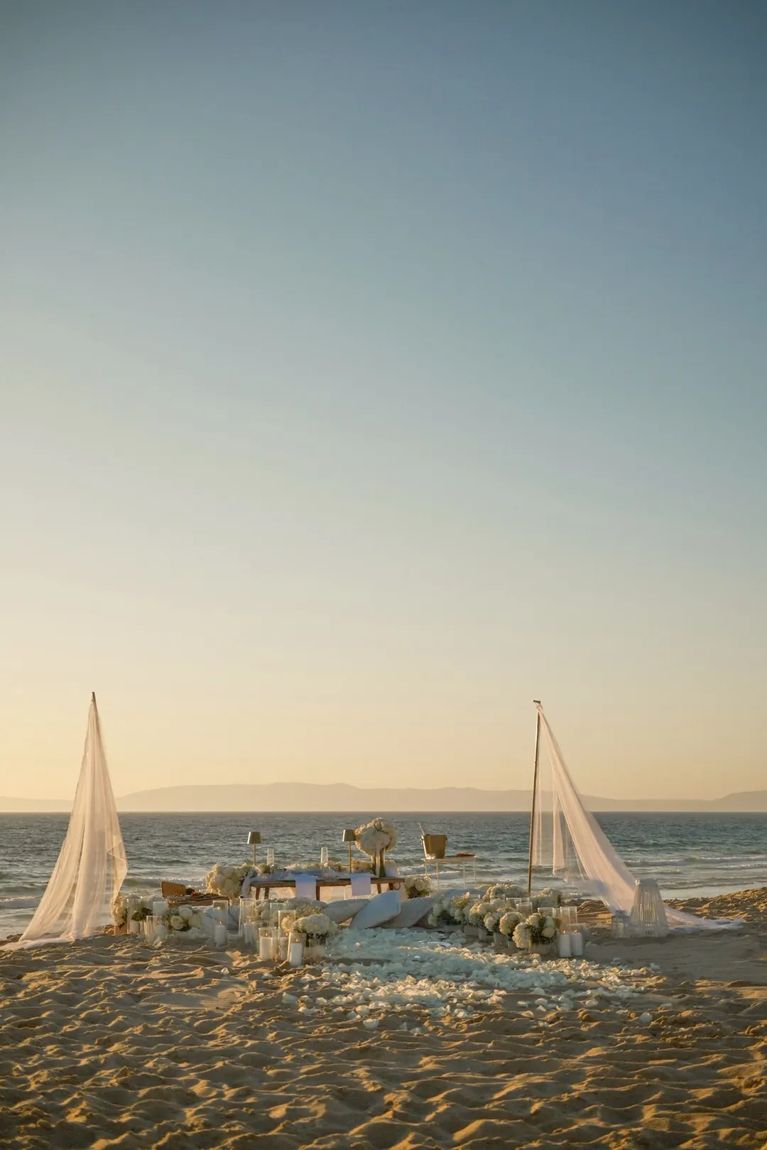 Two linen sails on the shore and a low table dressed with flowers facing the sea